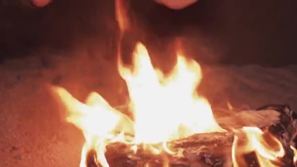 Mladý muž, posezení u ohně hořícího boty do písku na pobřeží — Stock video