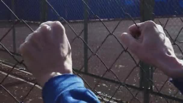 Mãos masculinas tocando cerca de arame de metal. jovem agressivo balançando malha de metal — Vídeo de Stock