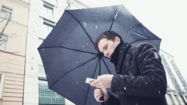 Erkek ceket ve smartphone kullanarak kar yağışı altında şemsiye ile örme atkı