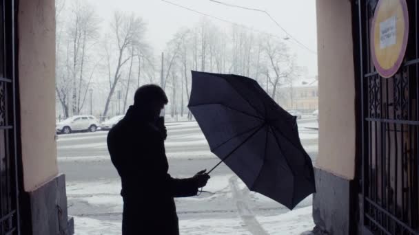 Silhouette eines Mannes, der bei Schneefall einen Regenschirm schließt. schneebedeckte Park Hintergrund — Stockvideo