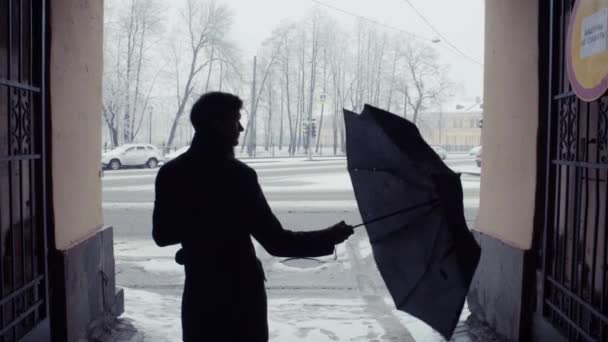 Silhouette of man opening umbrella under snowfall. Snow covered park background — Stock Video