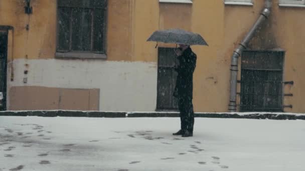 Homme en manteau avec parapluie debout sous la neige sirotant du café de tasse en plastique — Video