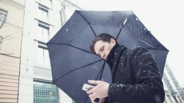 Ceket sokak üzerinde smartphone kullanarak kar yağışı altında şemsiye ile genç adam