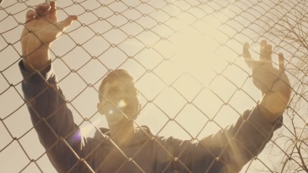 Caucasian young man in sports clothes standing breathing hard near metal fence — Stock Video