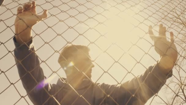 Caucasian young man in sports clothes standing breathing hard near metal fence — Stock Video