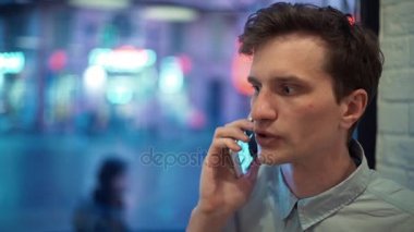 Mavi gömlekli akşam kafede telefonda konuşurken memnun genç adam