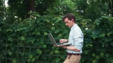 Genç adam dizüstü kulaklık kullanarak Park'ta yürüyüş ve bankta otur