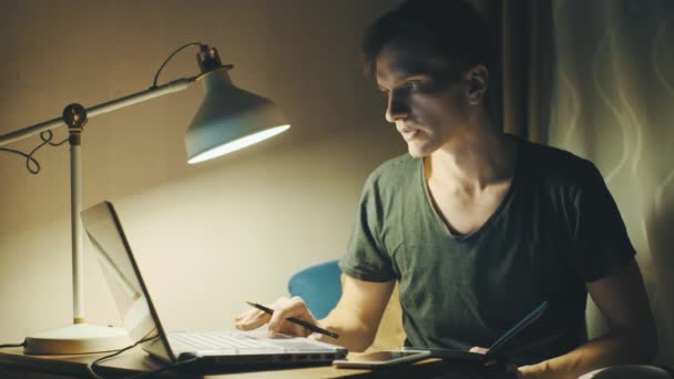 Hombre joven usando el ordenador portátil que tiene videollamada en casa por la noche — Vídeos de Stock