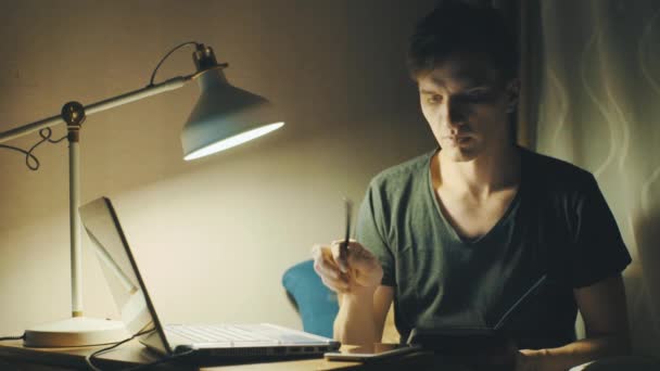 Young man using laptop having video call making notes in a notebook at home — Stock Video