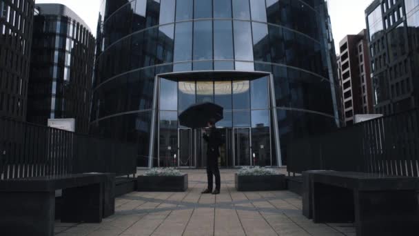 Jonge zakenman in pak staande met zwarte paraplu in de buurt van business-centrum — Stockvideo
