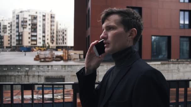 Mladý muž v obleku pomocí smartphonu. Rozestavěná budova na pozadí — Stock video