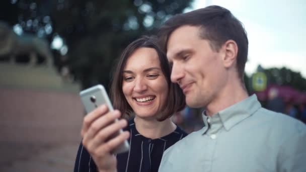 Feliz jovem casal milenar assistindo vídeos no smartphone juntos no parque — Vídeo de Stock