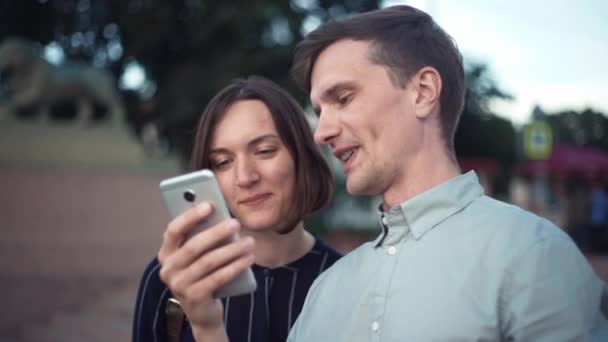 Feliz joven pareja milenaria utilizando el teléfono inteligente juntos en el parque — Vídeos de Stock