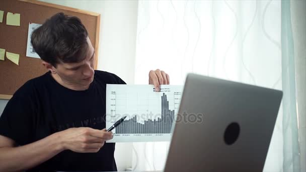 Freiberufler mit Videotelefonie am Laptop zeigt gedruckte Analysegrafiken — Stockvideo