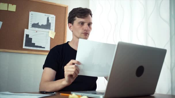 Jonge man aan het werk met analyseren grafieken in het kantoor aan huis — Stockvideo