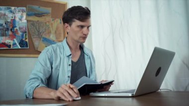 Casual giyimli yaratıcı adam ofiste dizüstü bilgisayar kullanır ve eskiz defteri içinde çizer