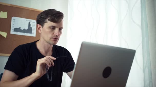 Δημιουργικός νεαρός άνδρας κρατά στα χέρια του γυαλιά, κοιτάξτε την οθόνη του φορητού υπολογιστή. — Αρχείο Βίντεο