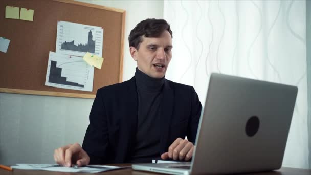 Joven hombre de negocios charlando con su socio de negocios utilizando el ordenador portátil — Vídeo de stock