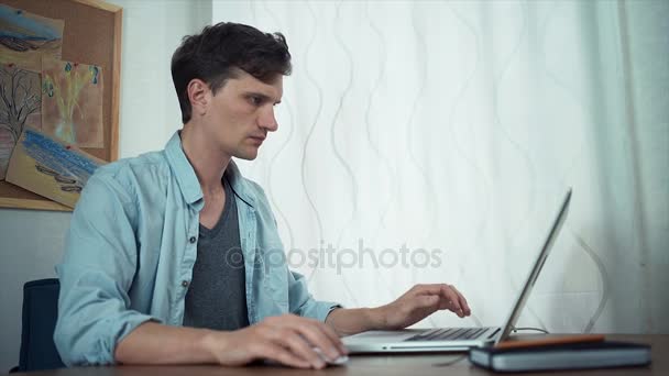 Freelancer usando laptop en la oficina. Tablero con bocetos de color en la pared detrás — Vídeos de Stock