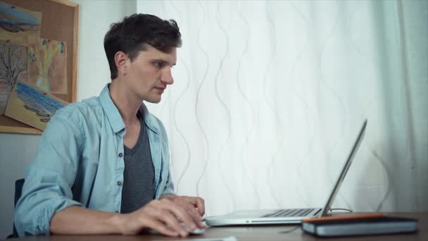 Young handsome man uses laptop makes notes in documents. Freelancer working home — Stock Video