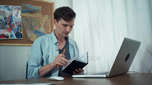 Genç bir adam fikri üstünde defter vasıl yazıhane yazı. Renkli çizimler, duvar ile kurulu — Stok video