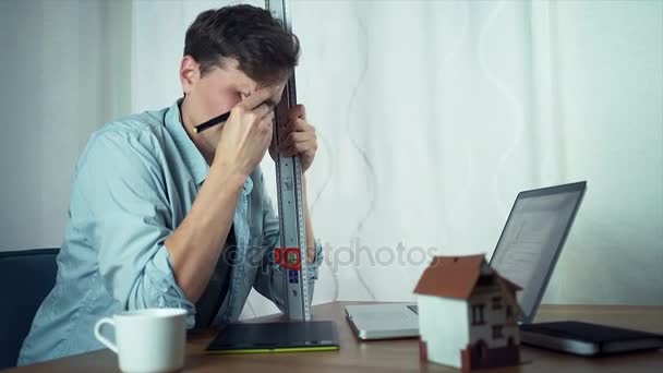 Joven diseñador cansado sentado frente a la computadora con una regla de metal . — Vídeos de Stock