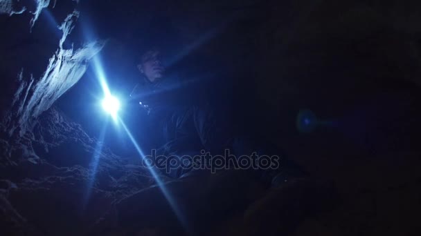 Guy utilisant smartphone posé sur le sol dans un trou étroit dans la grotte avec une lampe de poche — Video