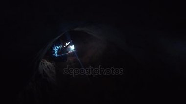 El feneri ile mağarada dar delikten dört ayak üzerinde dışarı karıştıran genç adam