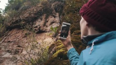 Smartphone ayakta bitki ve moss ile büyümüş yamaç yakınlarında kullanarak uzun yürüyüşe çıkan kimse