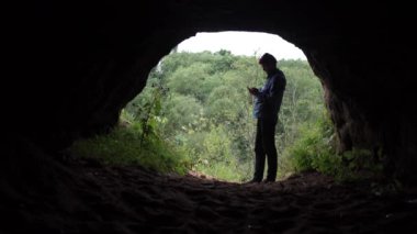 Gezgin Smartphone ayakta çıkış yakınındaki mağara kullanarak. Arka plan, orman.