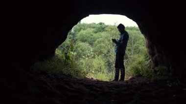 Adam uzun yürüyüşe çıkan kimse smartphone ayakta yakınındaki mağara çıkış. Arka plan, derin orman.