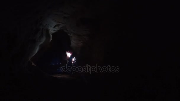 El hombre se revuelve en el agujero de la cueva ilumina el camino con la linterna en su teléfono inteligente — Vídeos de Stock