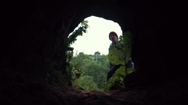 Νέοι πεζοπόρος εισέρχεται σε σκοτεινή σπηλιά κάτω από χαμηλό πέτρινο θόλο και με τα πόδια στο σκοτάδι — Αρχείο Βίντεο
