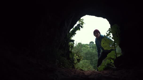 Молодой человек смотрит в темную пещеру с фонариком в руке . — стоковое видео