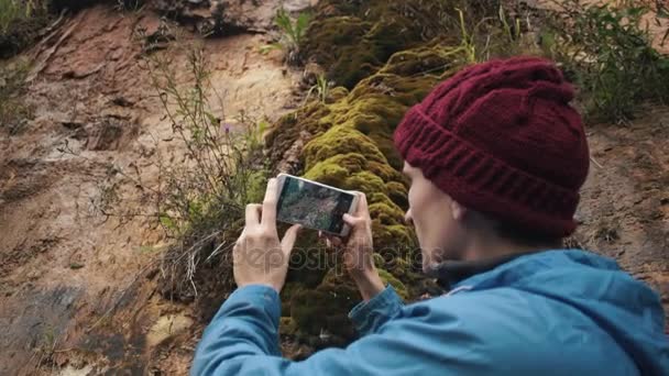 Viaggiatore con smartphone in piedi vicino al pendio ricoperto di piante e muschio — Video Stock