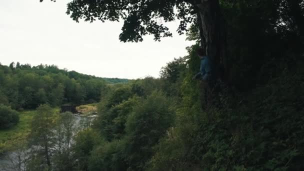 Wandelaar permanent aan rand van mount klampt zich vast aan de boom kijken naar landschap — Stockvideo