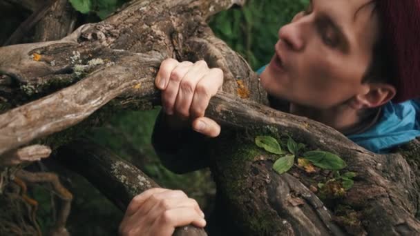 Young man climbs up top by slope clinging to the roots of trees — Stock Video