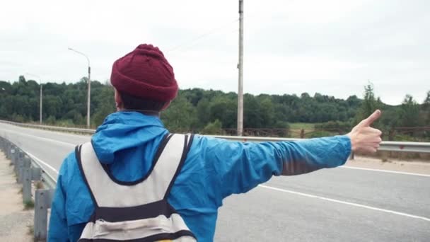 Viaggiatore vestito in giacca e cappello a maglia con zaino autostop su strada — Video Stock