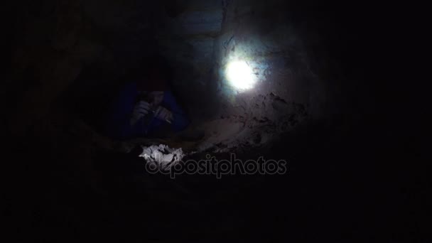 Человек протягивает руку, пытаясь взять фонарик, который лежит на земле в пещере — стоковое видео