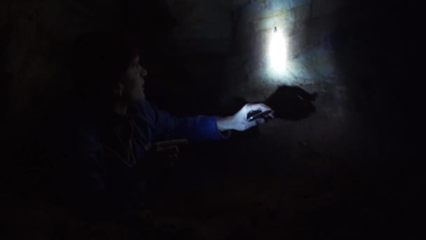 Turista na zem do úzké jeskyně zkoumá stěny jeskyně s ruční svítilna — Stock video