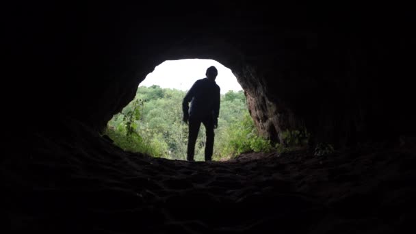 Joven explorador entra en la cueva oscura bajo la bóveda de piedra baja y camina hacia la oscuridad — Vídeos de Stock