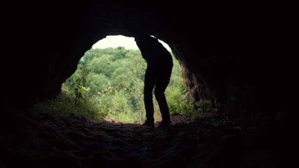 Mladý turista vyplouvá z temné jeskyně se zastaví a zvedá ruce nahoru — Stock video
