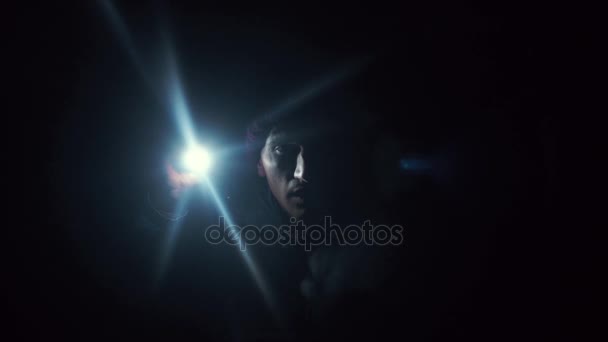 深い暗闇の中に立っている若い男が懐中電灯で闇を照らす — ストック動画