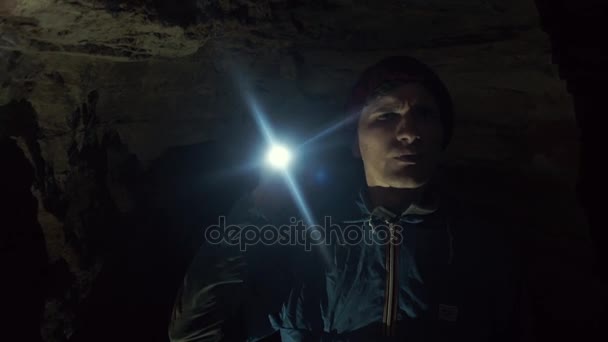 Jeune spéléologue debout dans une grotte étroite avec une lampe de poche à la main — Video