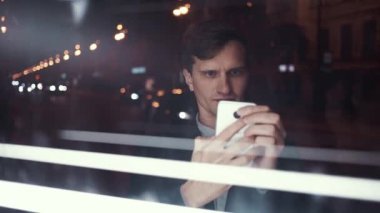 Genç yakışıklı adam akıllı telefon meşgul bir kentsel sokakta geceleri kullanarak.