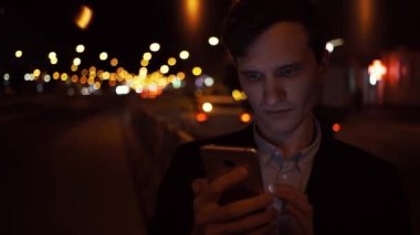 Yakışıklı genç adam giyiyor rahat elbise açık havada gülümseyen smartphone kullanarak