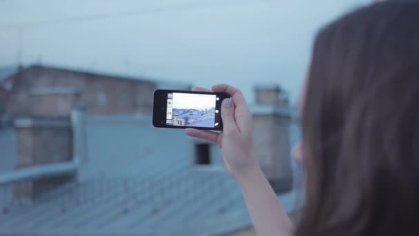 Chica joven tomando fotos con el teléfono inteligente sentado en el techo . — Vídeos de Stock