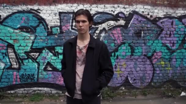 Un joven guapo parado junto a la pared del graffiti. Estilo de vida urbano — Vídeo de stock