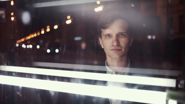 Junger lächelnder Mann blickt nachts allein auf belebte Stadtstraße in die Kamera — Stockvideo