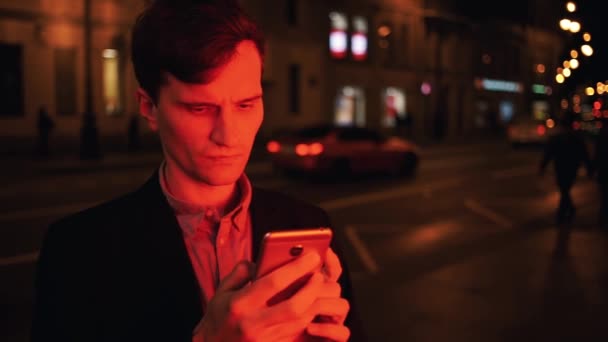 Portret van jonge man verlicht door rood licht met behulp van smartphone's nachts in de stad — Stockvideo